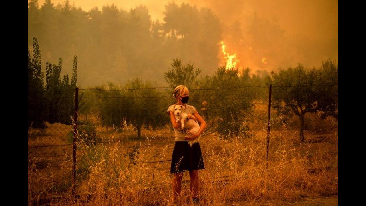 A woman holds a dog in her arms as forest fires approach the village of Pefki.
